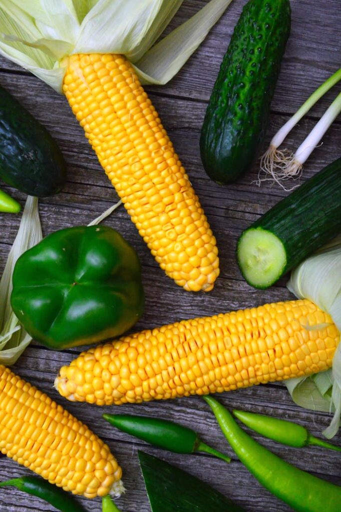 A vibrant assortment of fresh corn, peppers, and cucumbers on a wooden table.